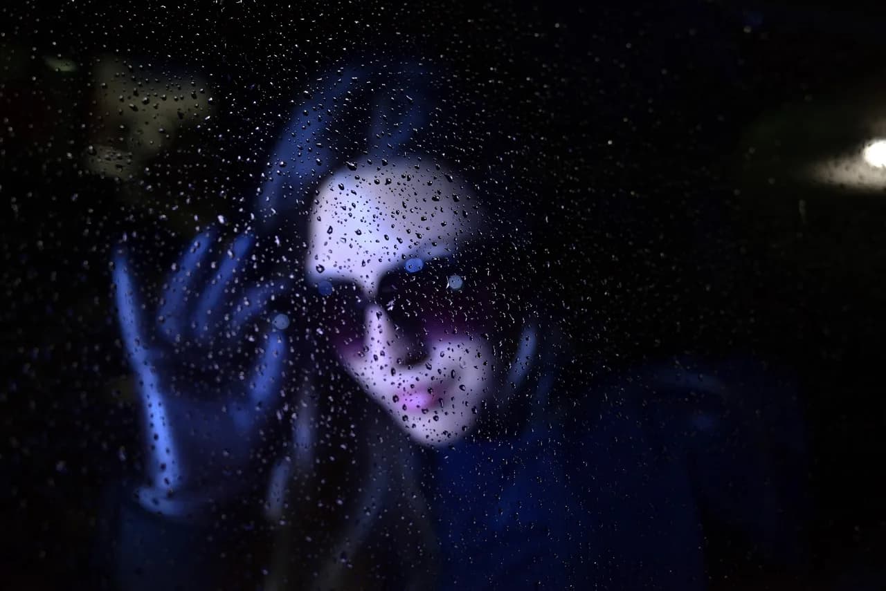 Frau hinter regennasser Scheibe bei Nacht in blauem Licht