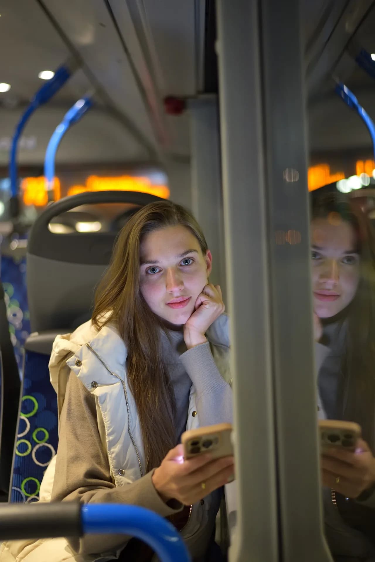 Junge Frau mit Smartphone im Bus bei Nacht mit Spiegelung