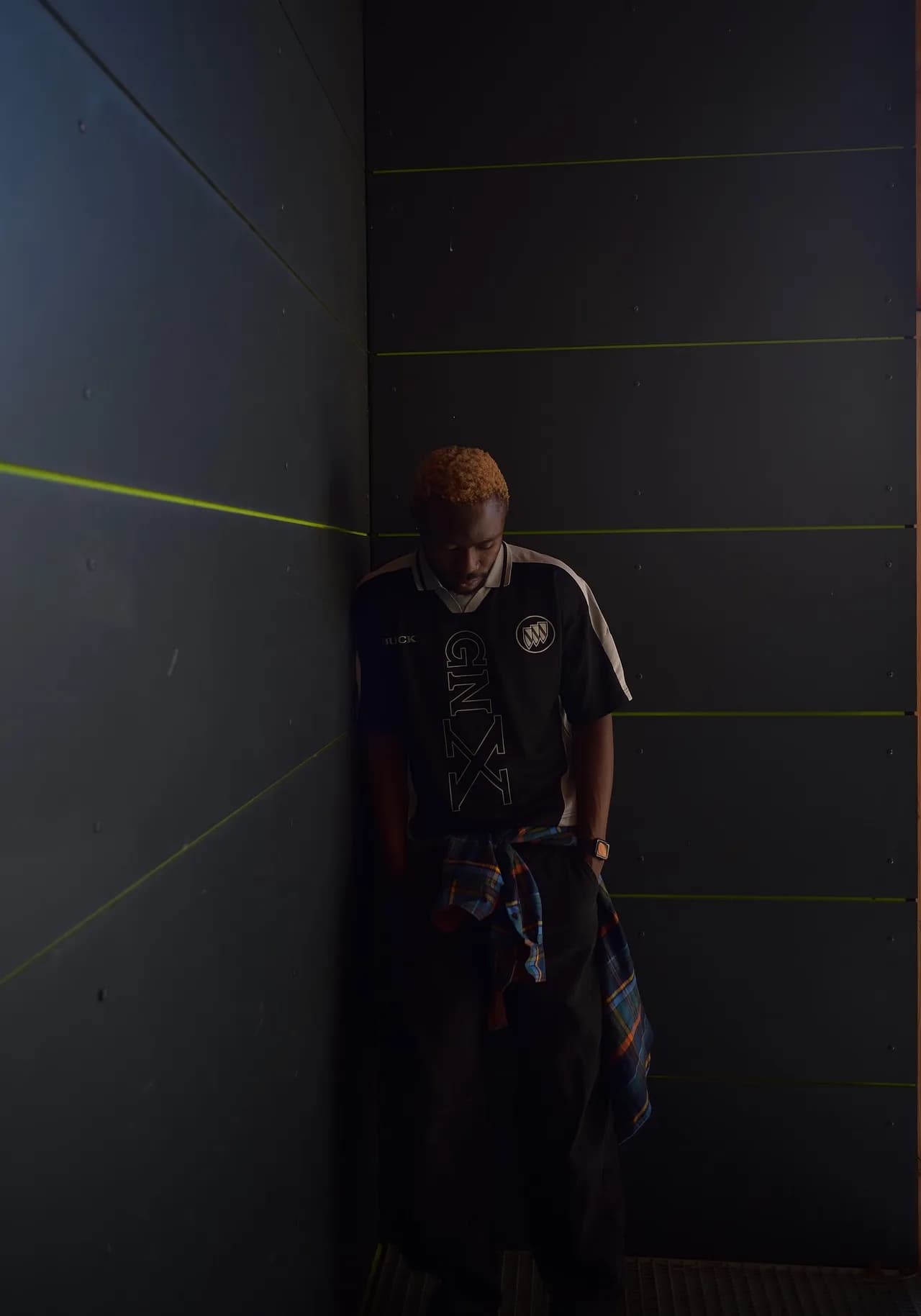 Mann im Trikot lehnt in einer dunklen Ecke mit gesenktem Blick