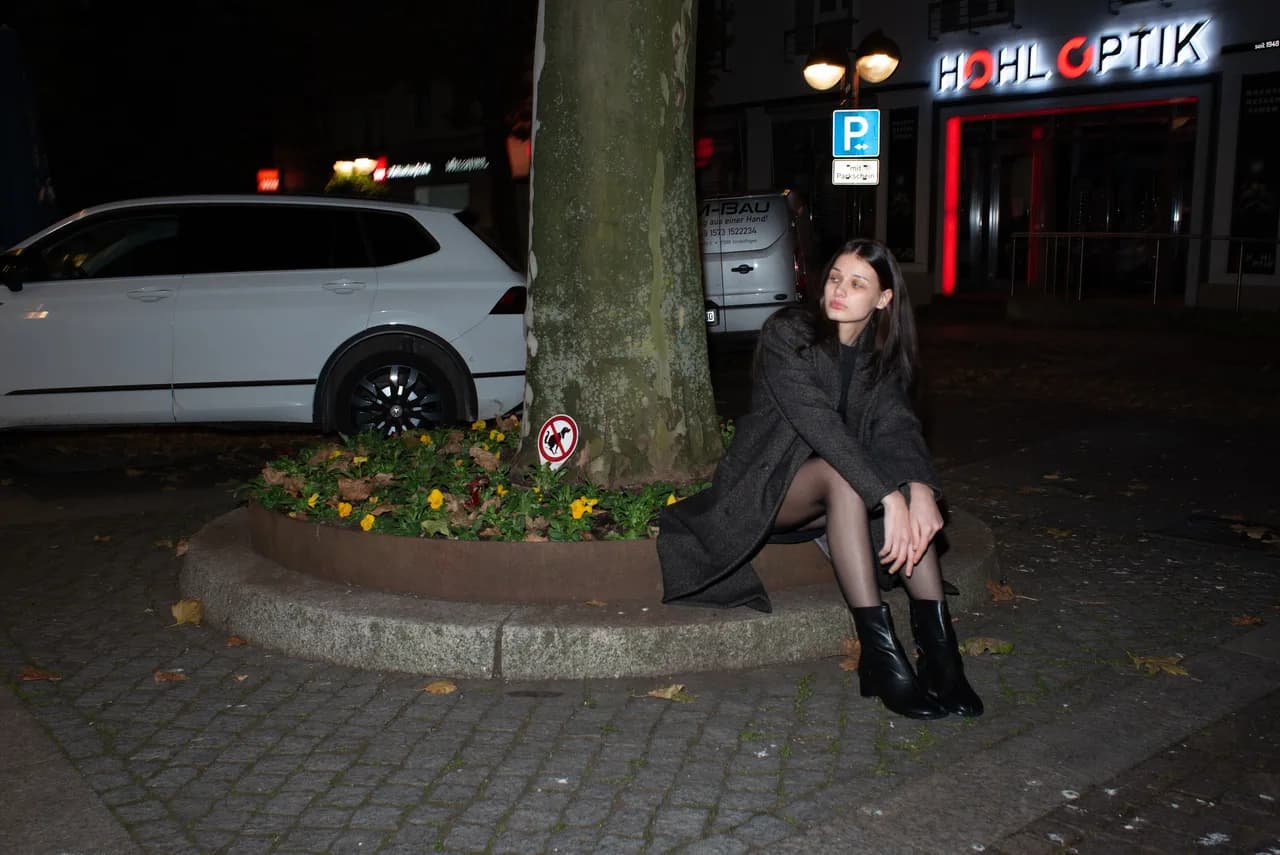 Frau sitzt nachts an einem Baum vor leuchtender Neonreklame