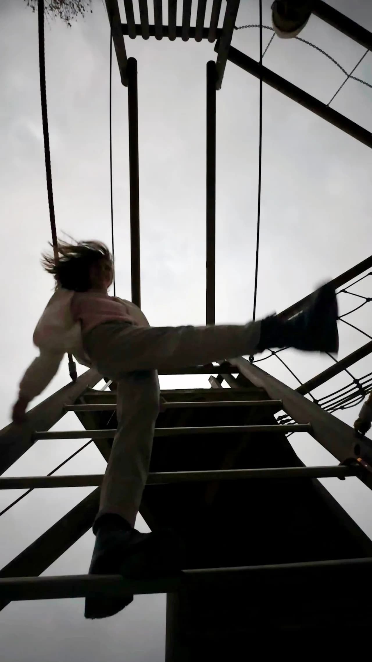 Silhouette einer kletternden Person auf einem Spielplatzgerüst vor grauem Himmel